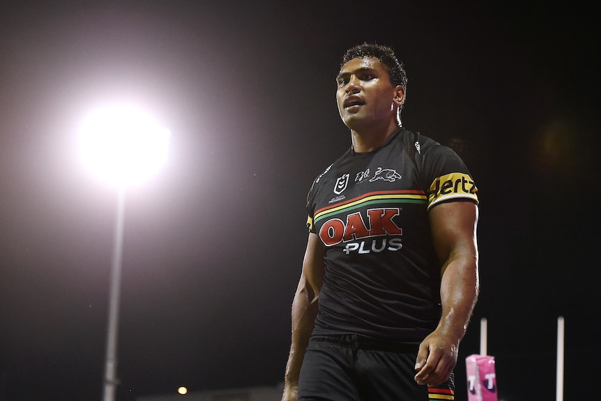 A man stands in silhouette in front of a floodlight during an NRL match