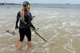 Woman walking into ocean with waterproof metal detector.