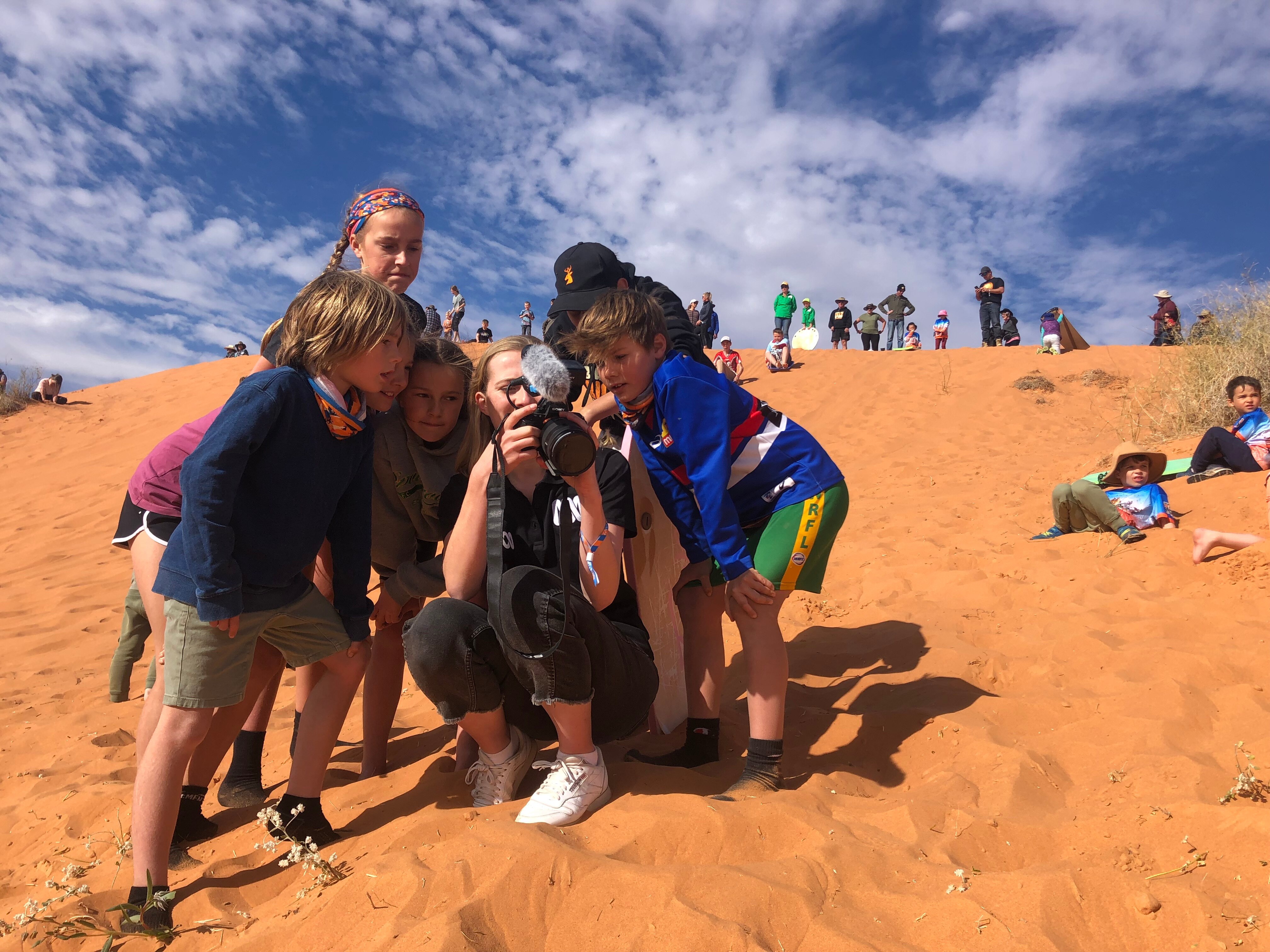 ABC reporter, with kids huddled around her, looking at photos on her camera.