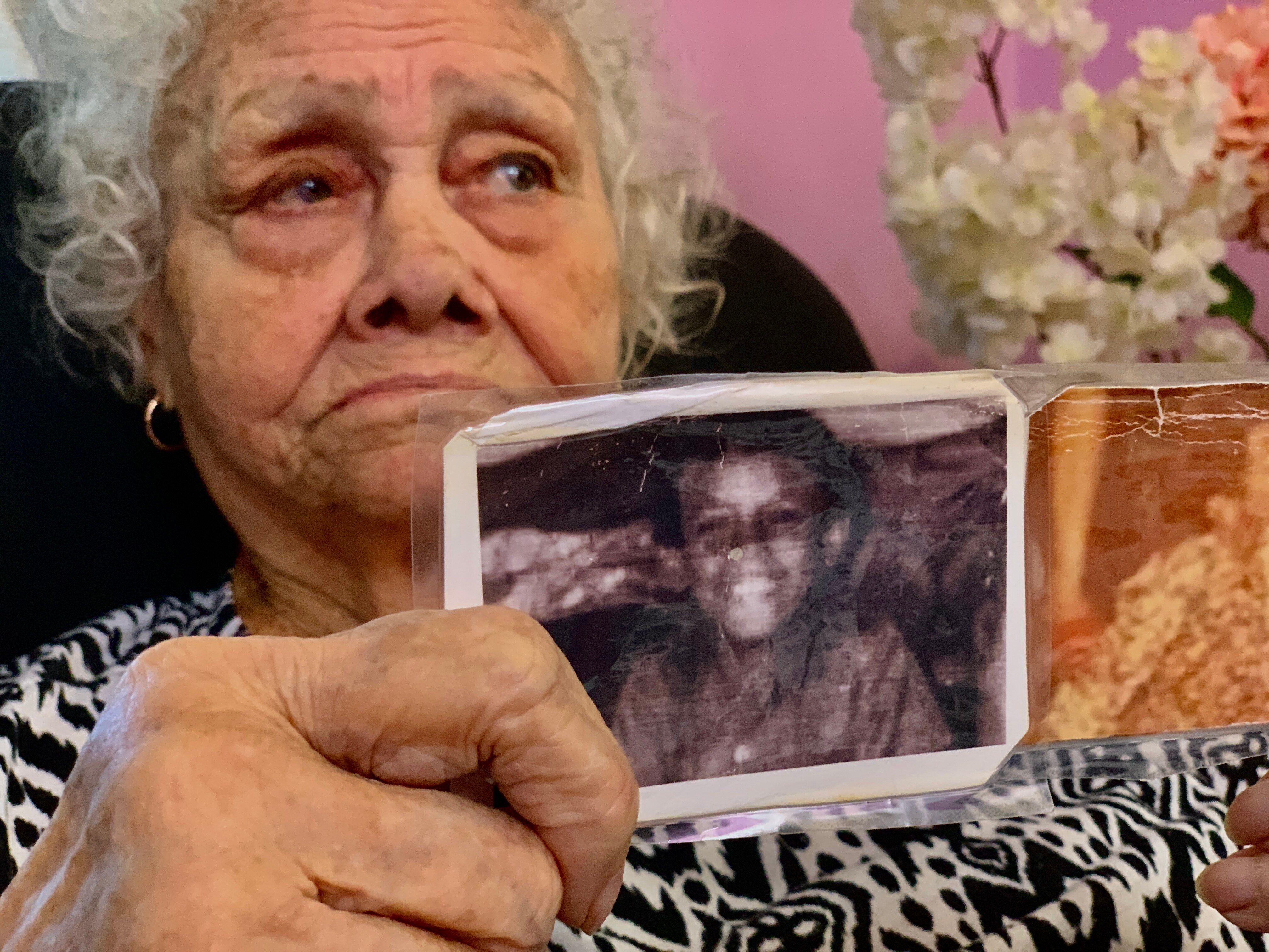 An elderly lady holds up two faded photos of a small, smiling boy