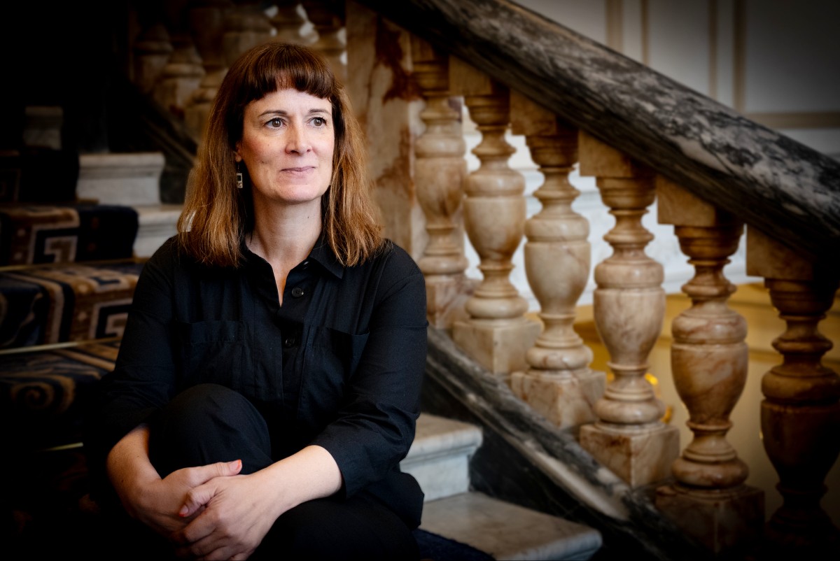 Uma mulher sentada com as mãos nos joelhos, olhando.