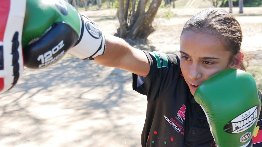Aboriginal girl with green boxing gloves practicing with police in a park in Bundaberg, Queensland.