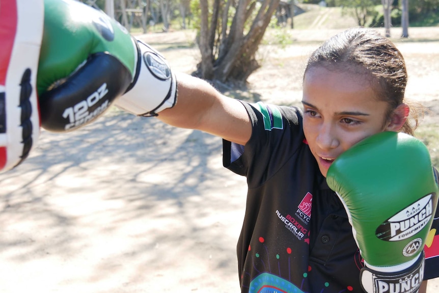 Aboriginal girl with green boxing gloves practicing with police in a park in Bundaberg, Queensland.