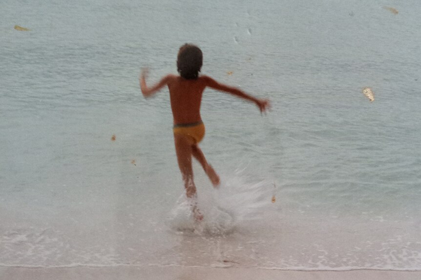 A photo shows a child from behind running into the water at the beach.