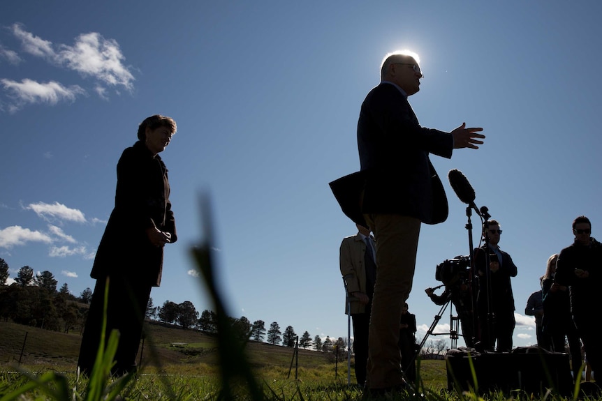 A low side angle silhouette shot of Morrison standing at a microphone gesticulating with his right hand. Kotvoys standing behind