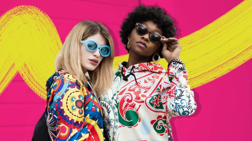 Two women pose with sunglasses and bright clothing against a pink wall for a story about how to accessorise.