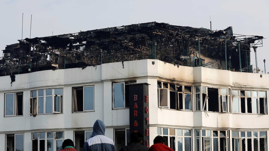 Onlookers stand on the rooftop of a building as they look at a hotel where a fire broke out in New Delhi