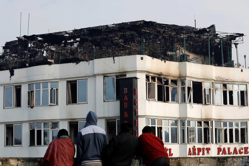 Onlookers stand on the rooftop of a building as they look at a hotel where a fire broke out in New Delhi