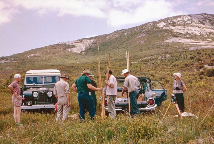 A wide of various people in front of historic vehicles