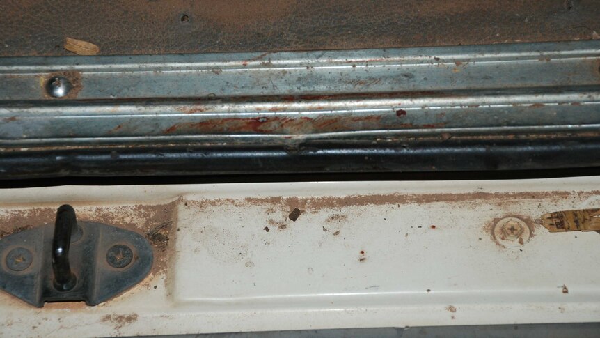 A close-up of the door of a van shows a red blood smear.