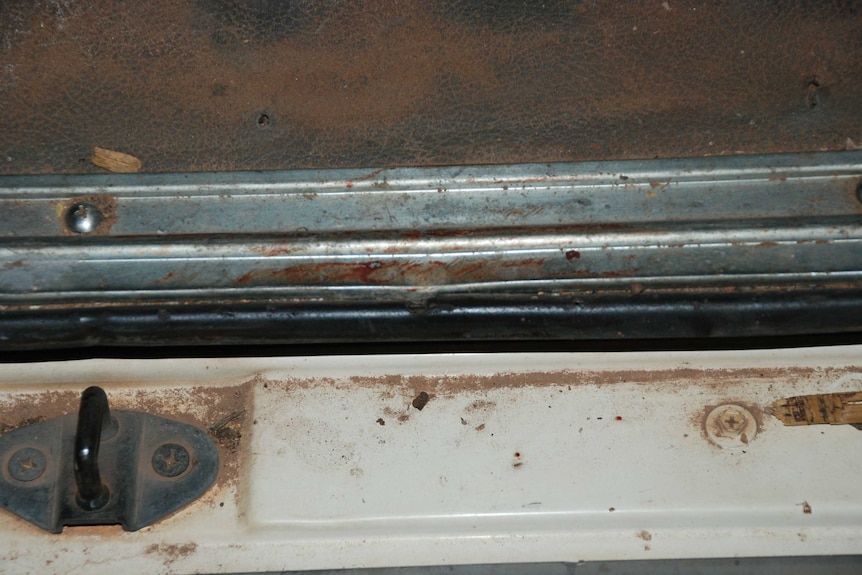 A close-up of the door of a van shows a red blood smear.