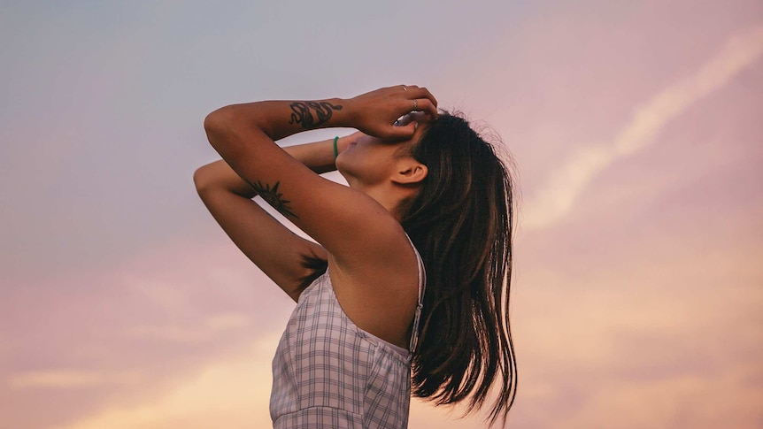 Woman with hands raised looking up to a pink blue sunset sky, in a story about talking about mental illness in Asian families.