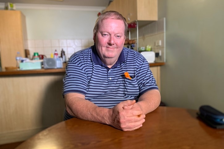 Michael Powel sits at a table with his hands clasped together, his kitchen is in the background