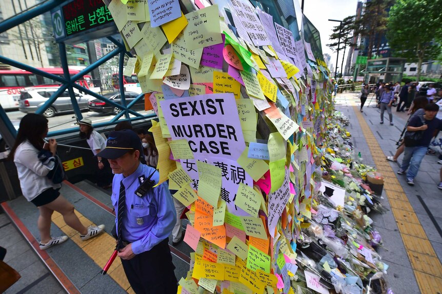 A guard standing at the entrance of Exit 10 at Gangnam Station next to a wall of multicoloured post-it notes.
