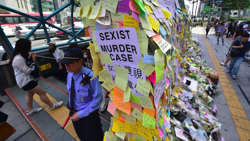 A guard standing at the entrance of Exit 10 at Gangnam Station next to a wall of multicoloured post-it notes.