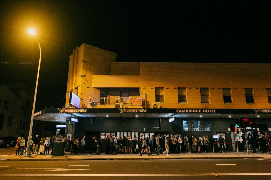 A line of gig punters queue down Hunter Street in Newcastle outside The Cambridge Hotel at night