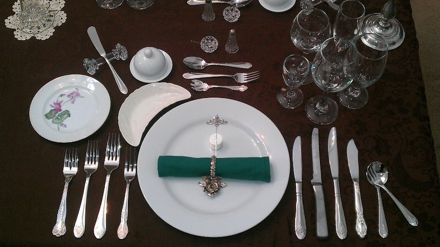 A 12 course table setting with a plate, many pairs of cutlery and several types of wine glasses.