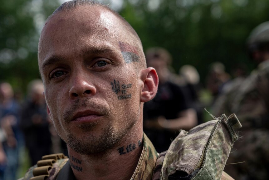 A fighter of Russian Volunteer Corps with face tattoos and a shaved head walks to his vehicle.