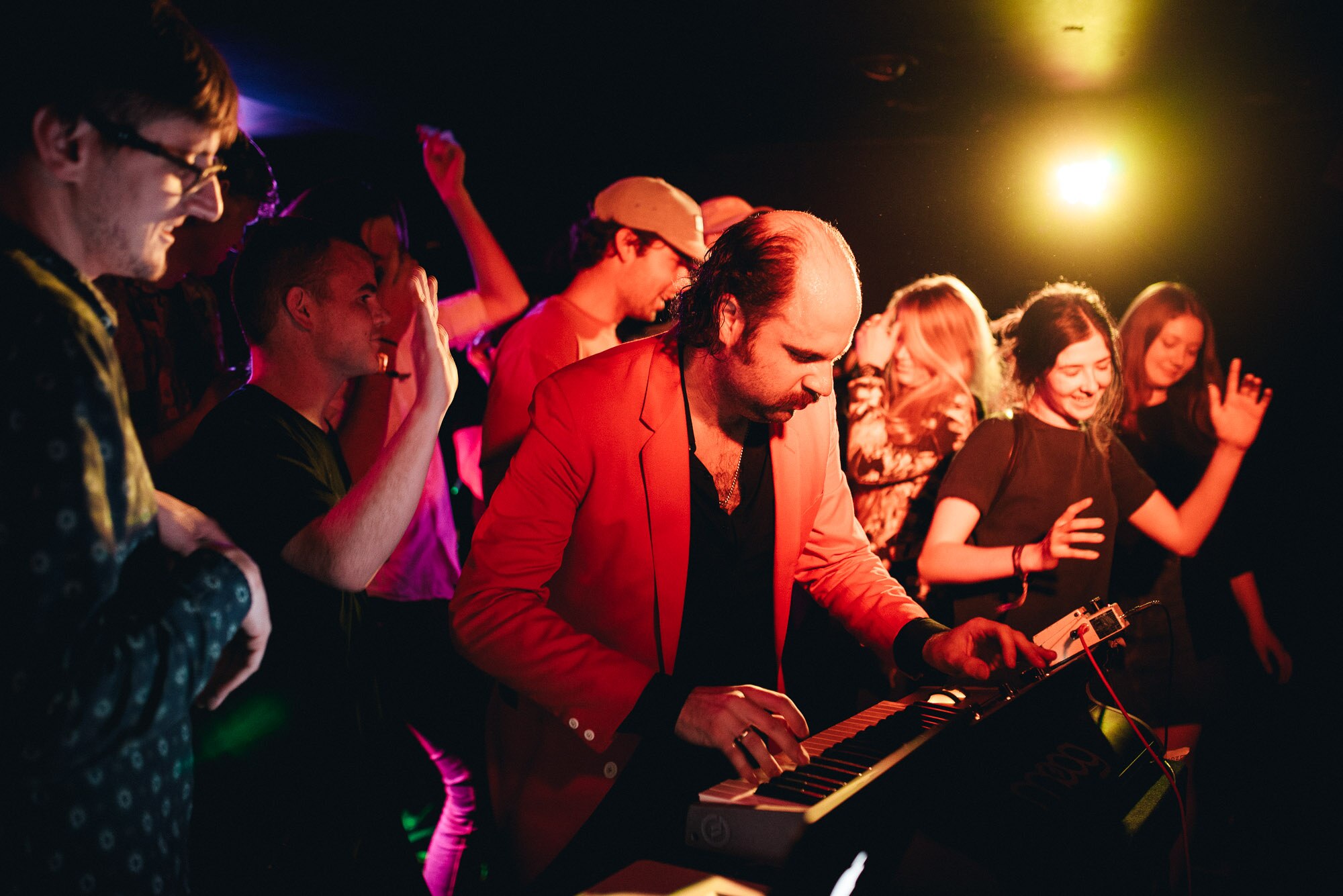 A man plays a keyboard on stage, surrounded by young dancing people