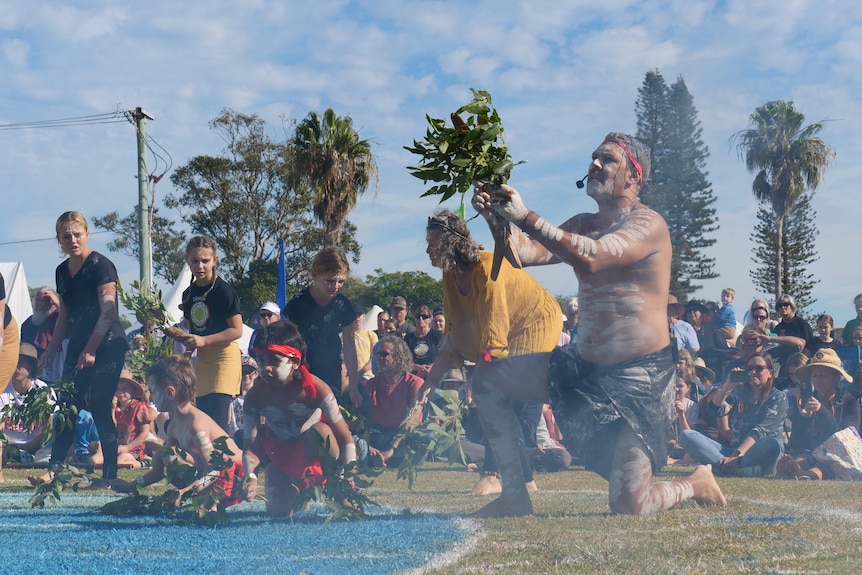 Male Aboriginal dancers, in traditional dress and body paint, perform outdoors, featuring men and boys.
