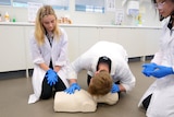 Three students kneeling over a CPR doll while one gives mouth to mouth.