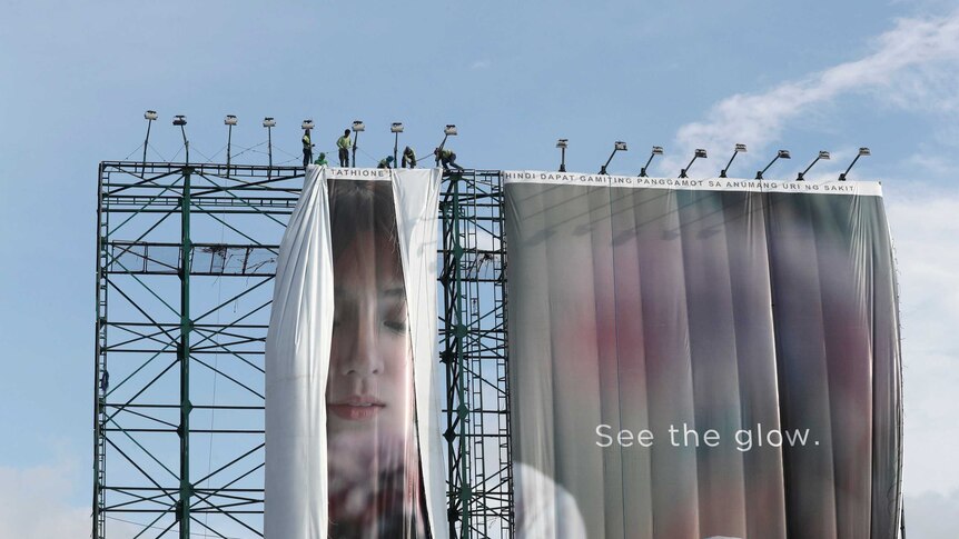 Workers stand above a large advertising billboard to remove it