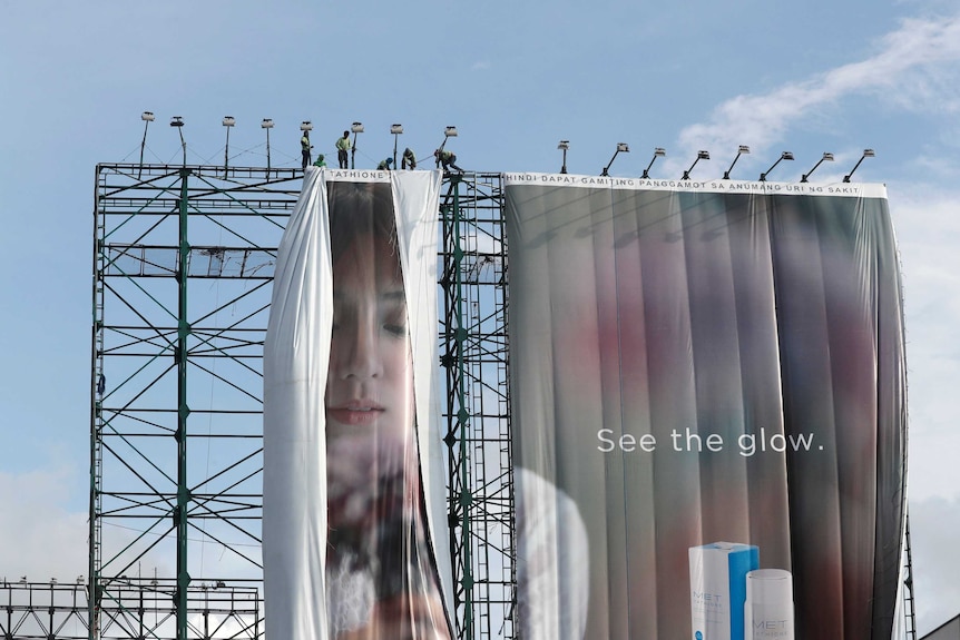 Workers stand above a large advertising billboard to remove it