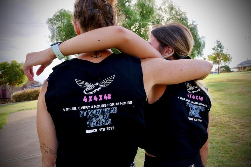 two women facing the back with their arms around each other and a black t-shirt with a staying home leaving violence logo