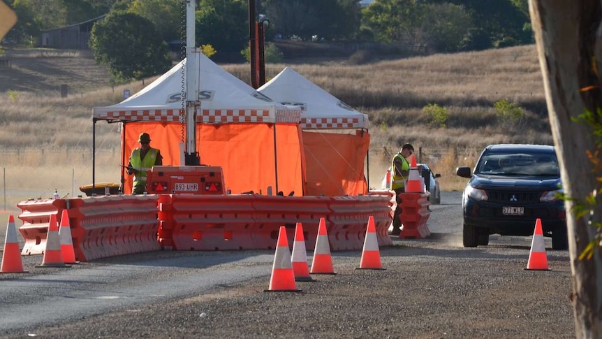 Two men in high vis vests stand under SES tents at the checkpoint as a car drives up to enter Cherbourg.