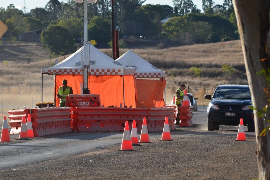 Two men in high-vis vests stand under SES tents at a checkpoint as a car drives up.