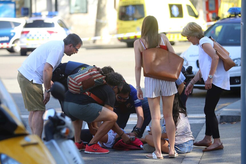 A crowd of people helps a person lying on the street.