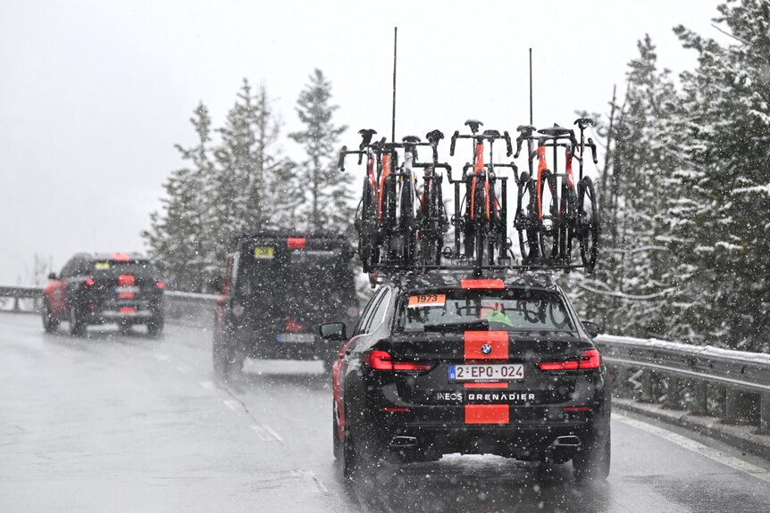 A car has bikes on its roof as it drives along a snowy mountain