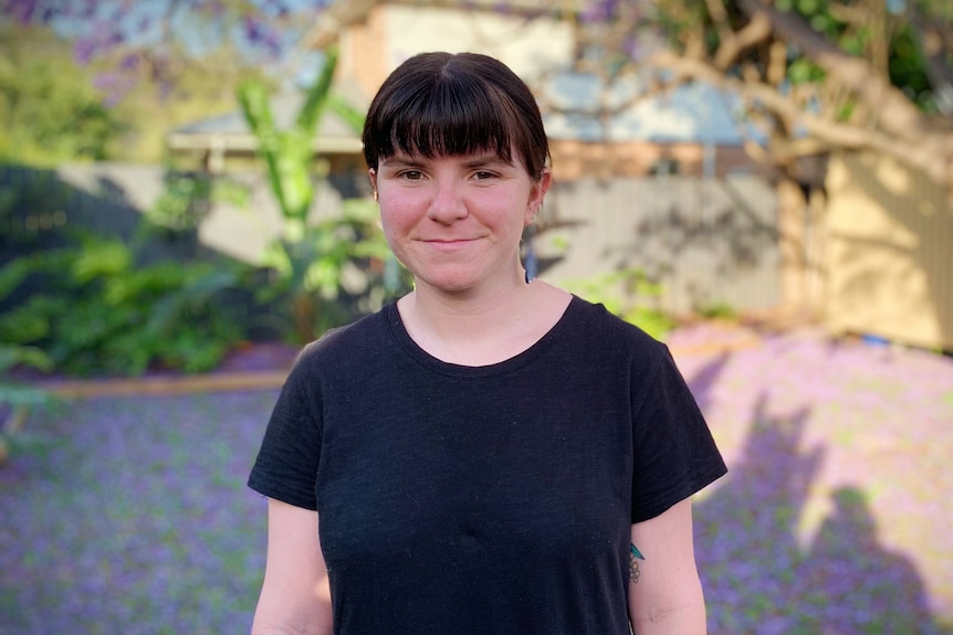 A young woman in a black t-shirt smiles in a backyard