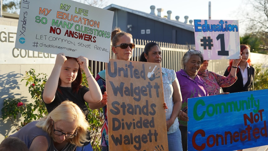 A group of women stand outside a school entrance with protest signs