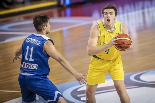 Man in Australian basketball uniform holding ball with defender in blue