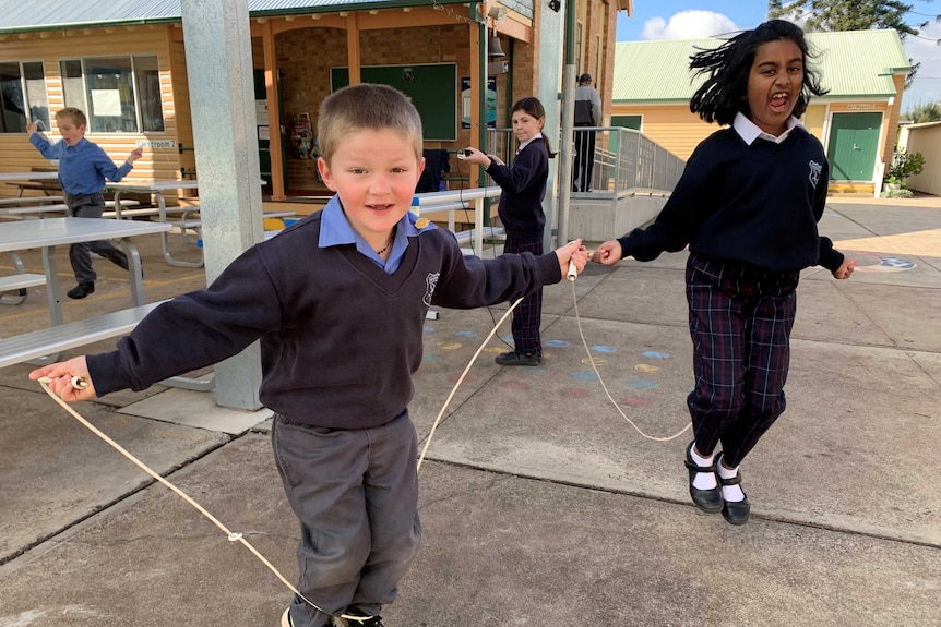 A boy and girl in school uniform play with skipping ropes.