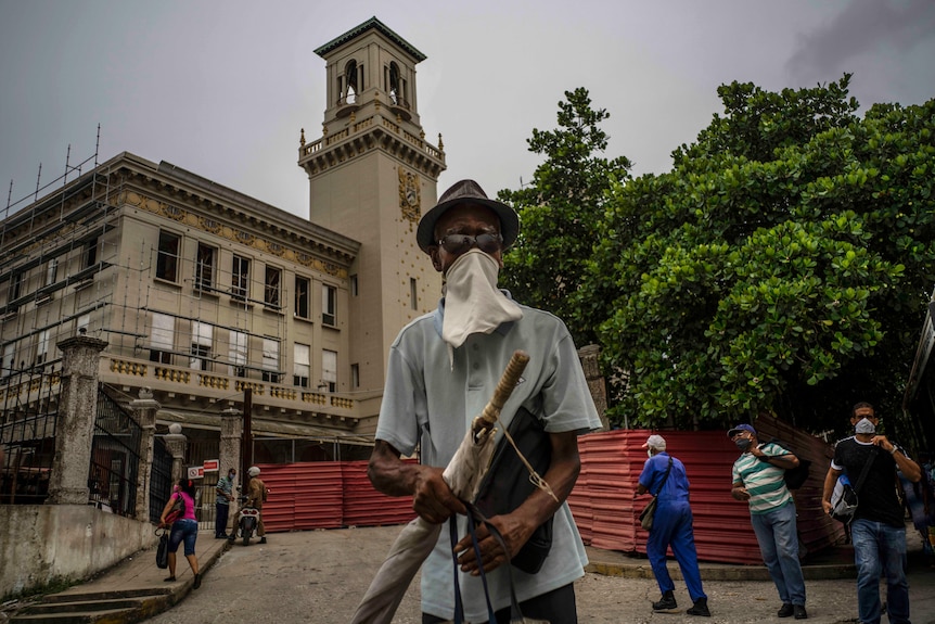 A man wearing a makeshift face mask and glasses stands outside a train station in Havana, Cuba