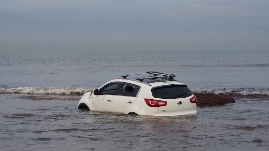 A white car submerged in beach water