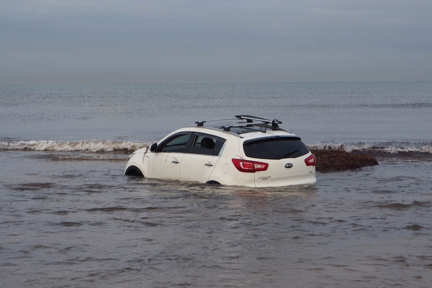 A white car submerged in beach water