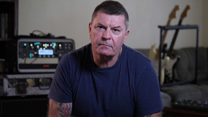 Portrait of a man looking at he camera with guitars and an amplifier in the background