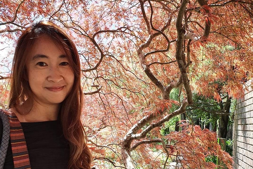 A woman smiling outside against a leafy background.