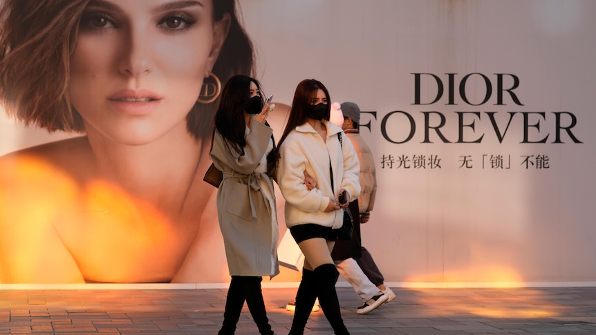 Women wearing masks walk past an ad for Dior at a mall in Beijing, China, 