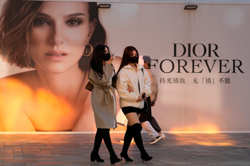 Women wearing masks walk past an ad for Dior at a mall in Beijing, China, 