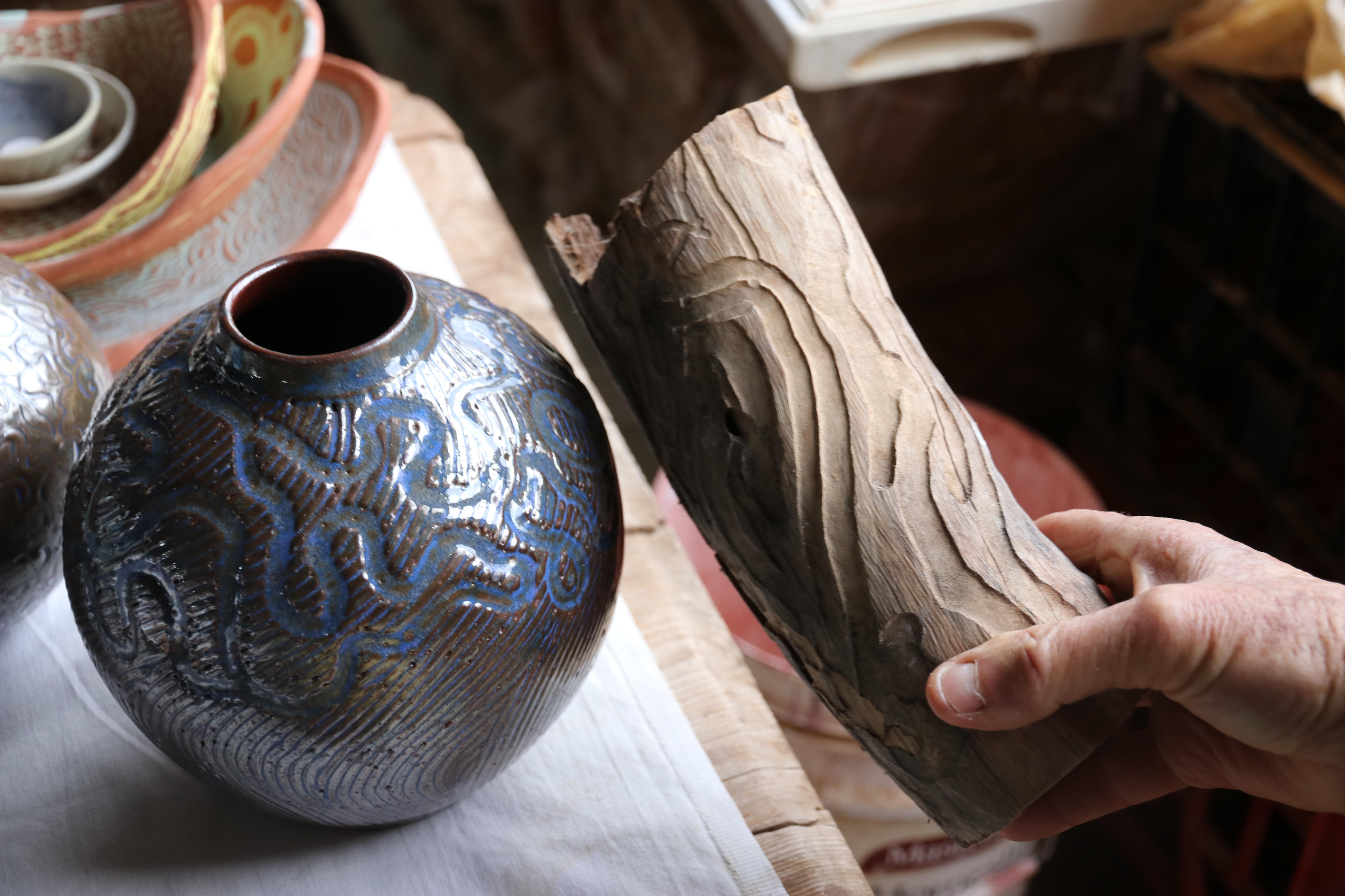 woman holds a piece of a log next to a ceramic vase with the same pattern