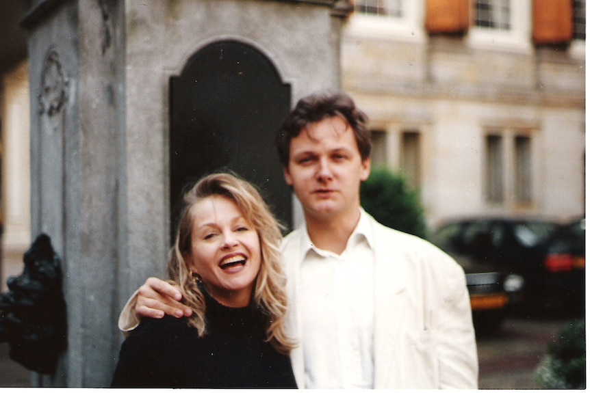 A young blonde woman laughing next to a blonde man in a white suit on the street in Europe.