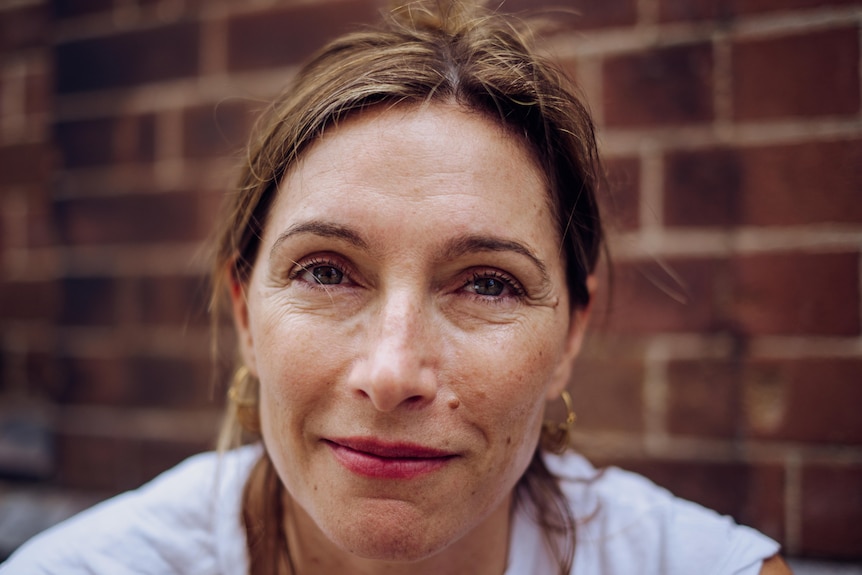 A close-up portrait of Claudia Karvan, gazing past the camera, with a brick wall behind.