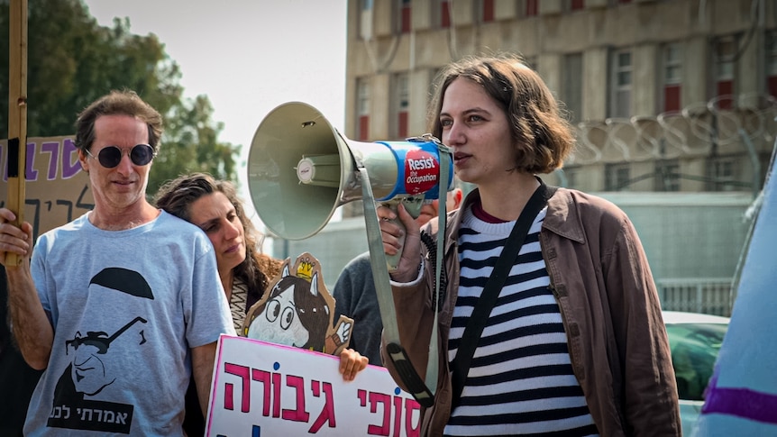 A teenager with a brown bob speaks into a megaphone 