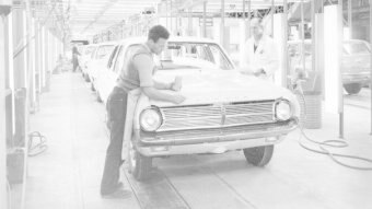 A man polishes the bonnet of a Holden car inside a factory in a production line.
