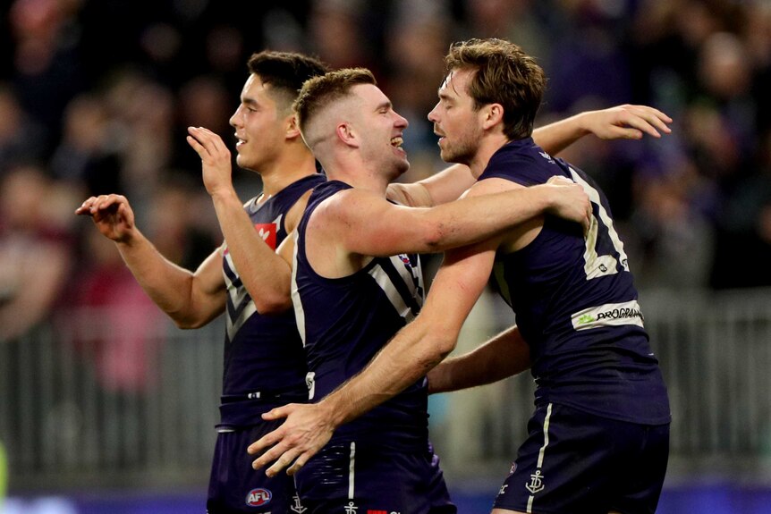 AFL players embrace after winning a close game.