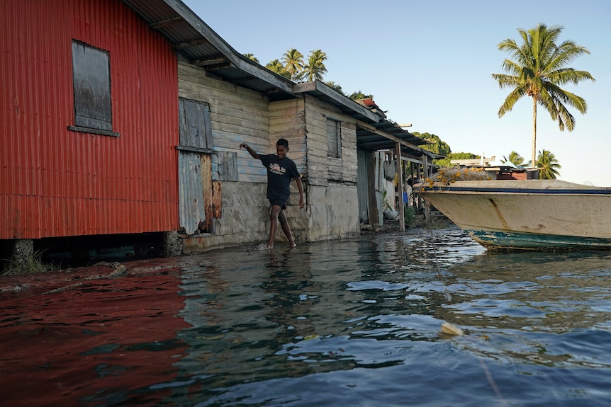 A little boy wading through the water next to a house that was flooded by the sea